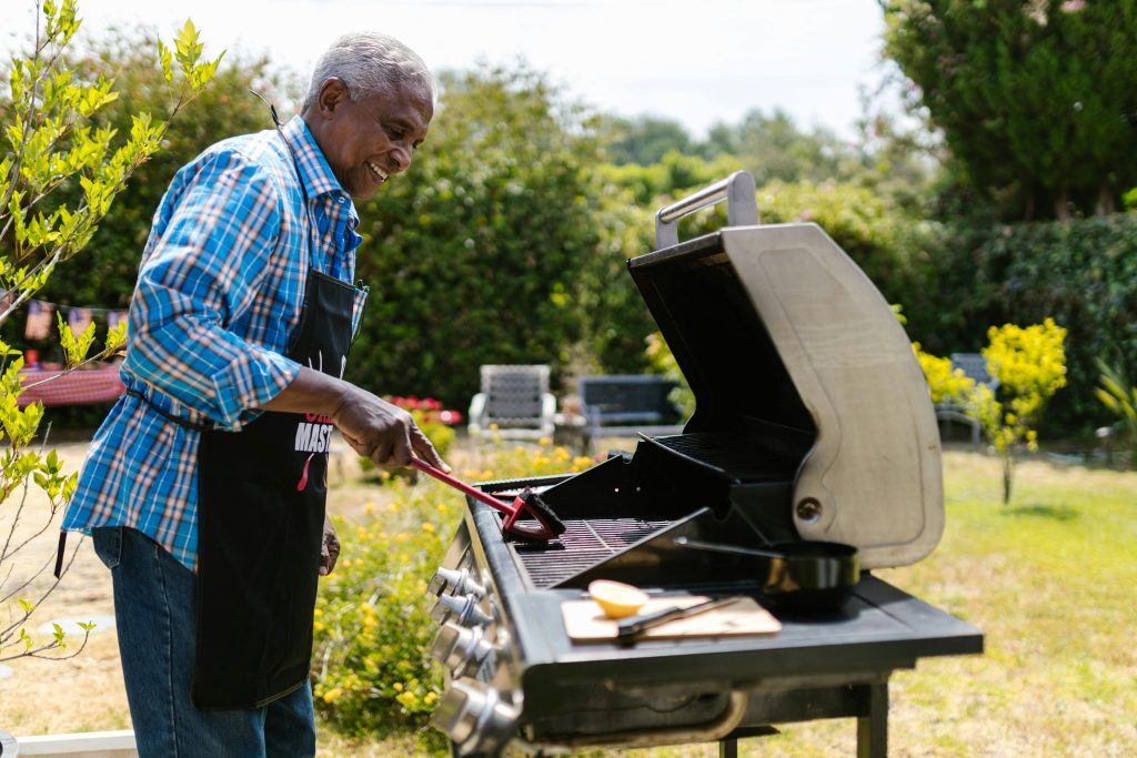 Elderly man enjoying barbecuing outdoors surrounded by greenery and garden ambiance.